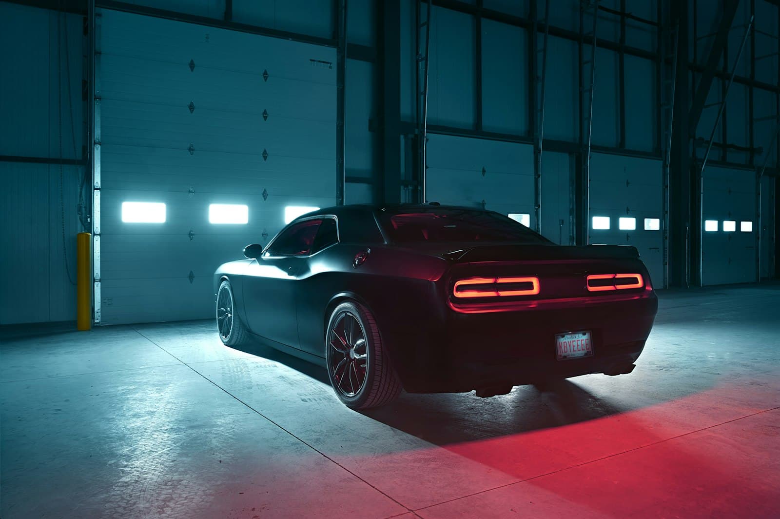 Voiture noire dans un hangar industriel, feux arrière rouges